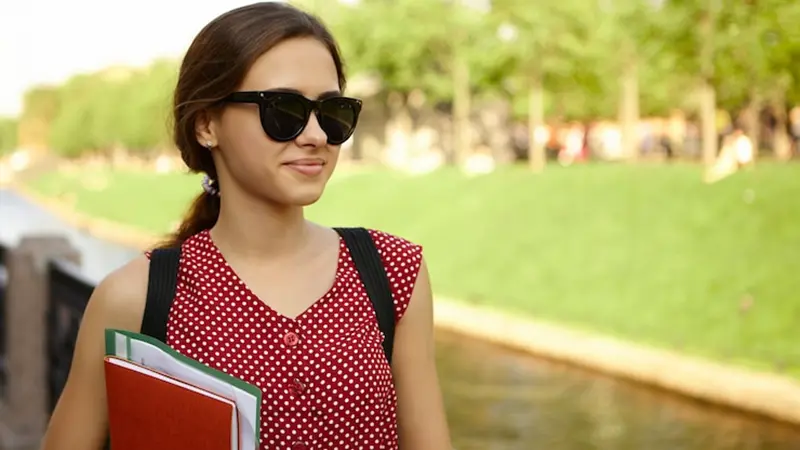 Services for people with vision loss showing a female college student with books walking on campus.